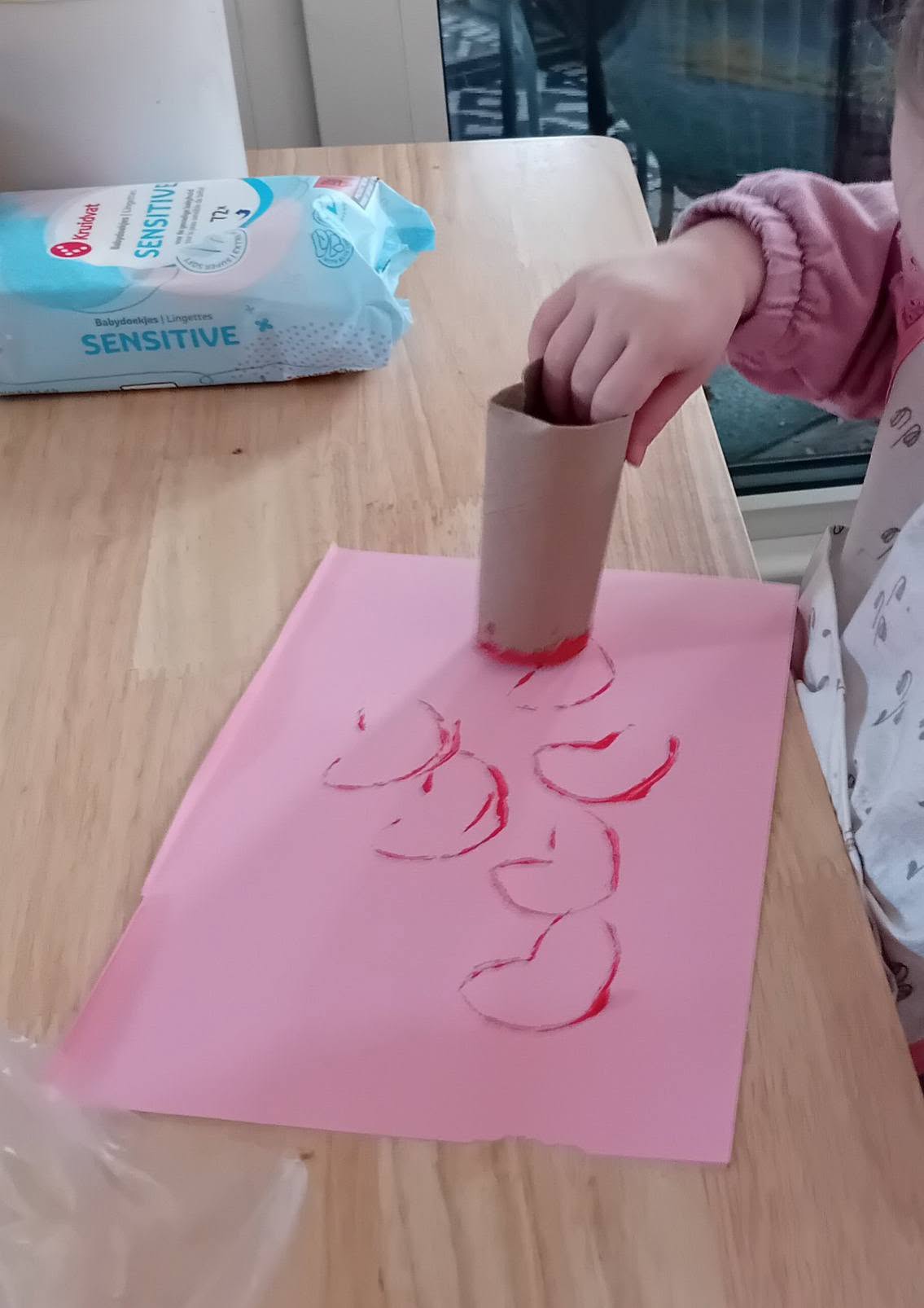 Kind stampt hartjes met verf op roze papier