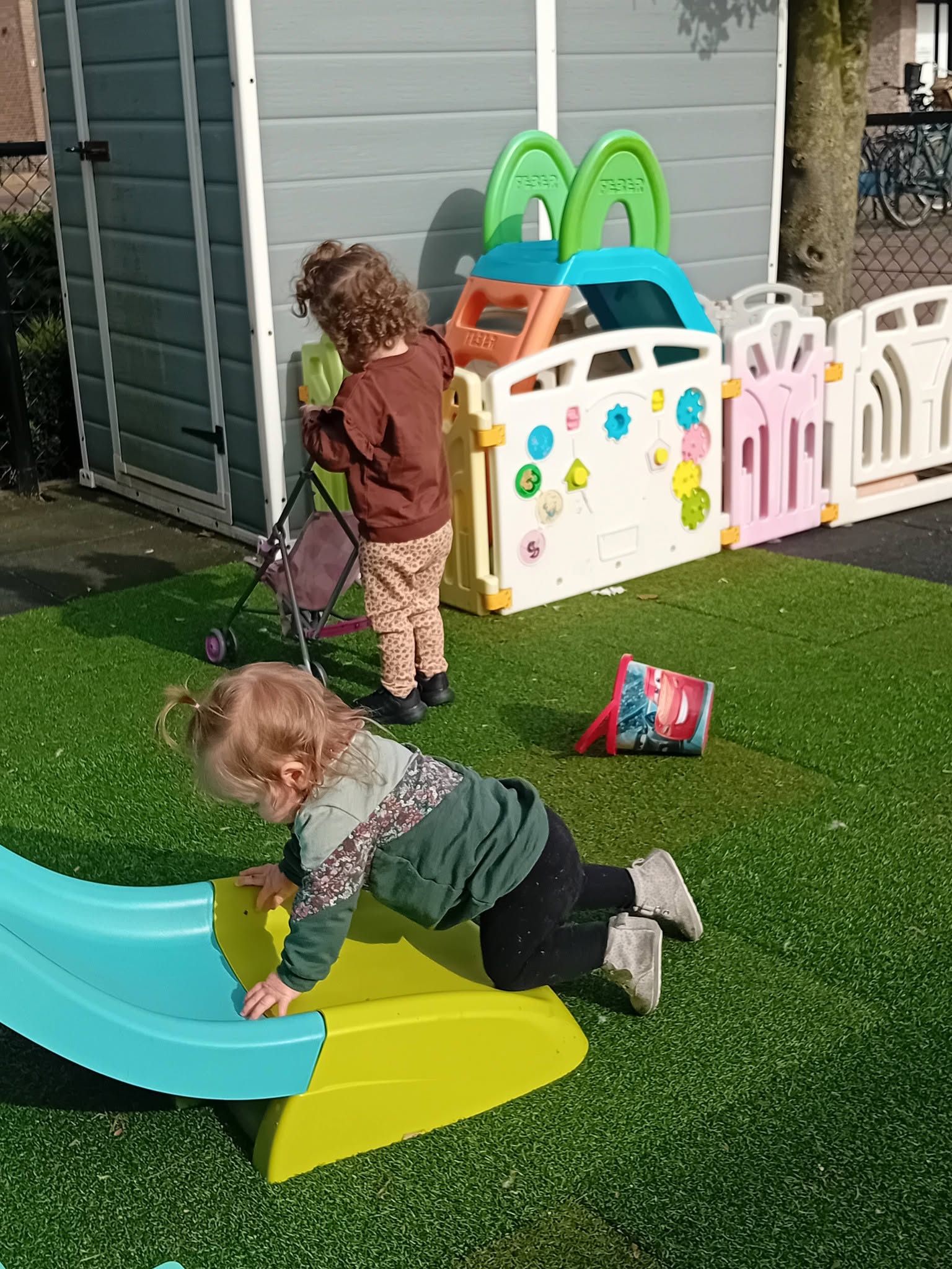 Kinderen spelen op kunstgras bij het speeltoestel en de glijbaan